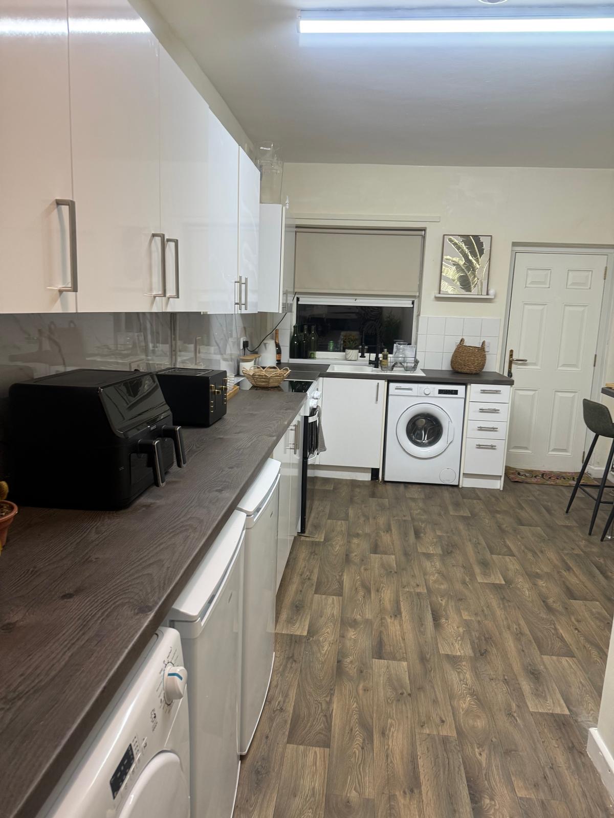 Kitchen after: bright white units, fresh flooring, calm wide layout