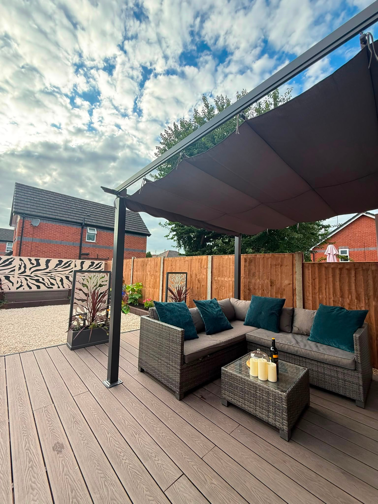 The pergola seating area up close: rattan sofa with teal cushions under a grey canopy