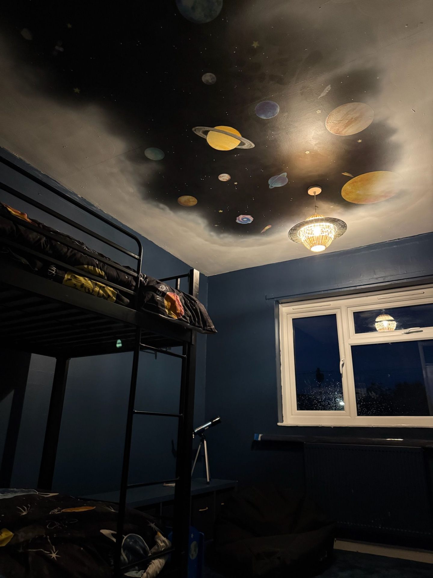 Space-themed bedroom at night: planets glowing across the painted ceiling