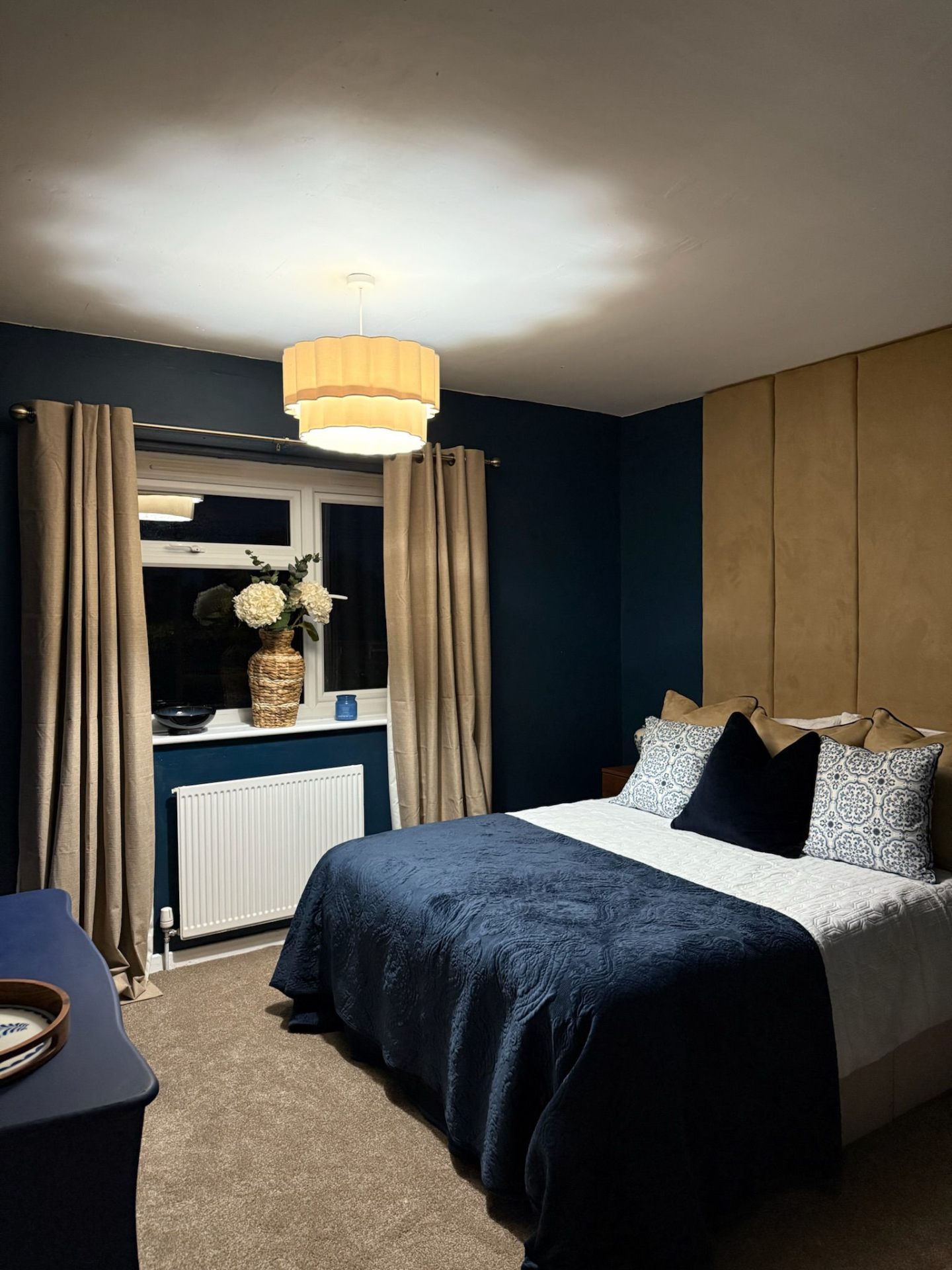 Sarah's bedroom after: deep navy walls, gold velvet upholstered headboard and warm pendant lighting