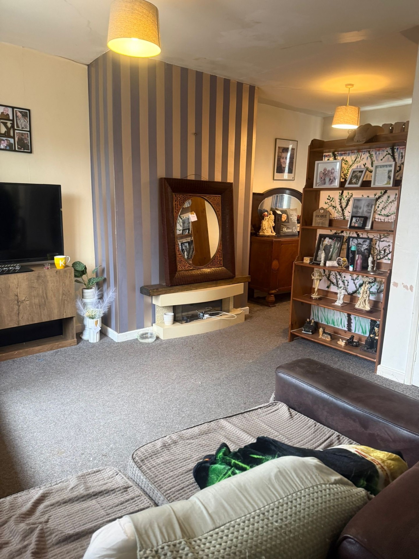 Living room before: striped feature wall, dated fireplace, cluttered shelving
