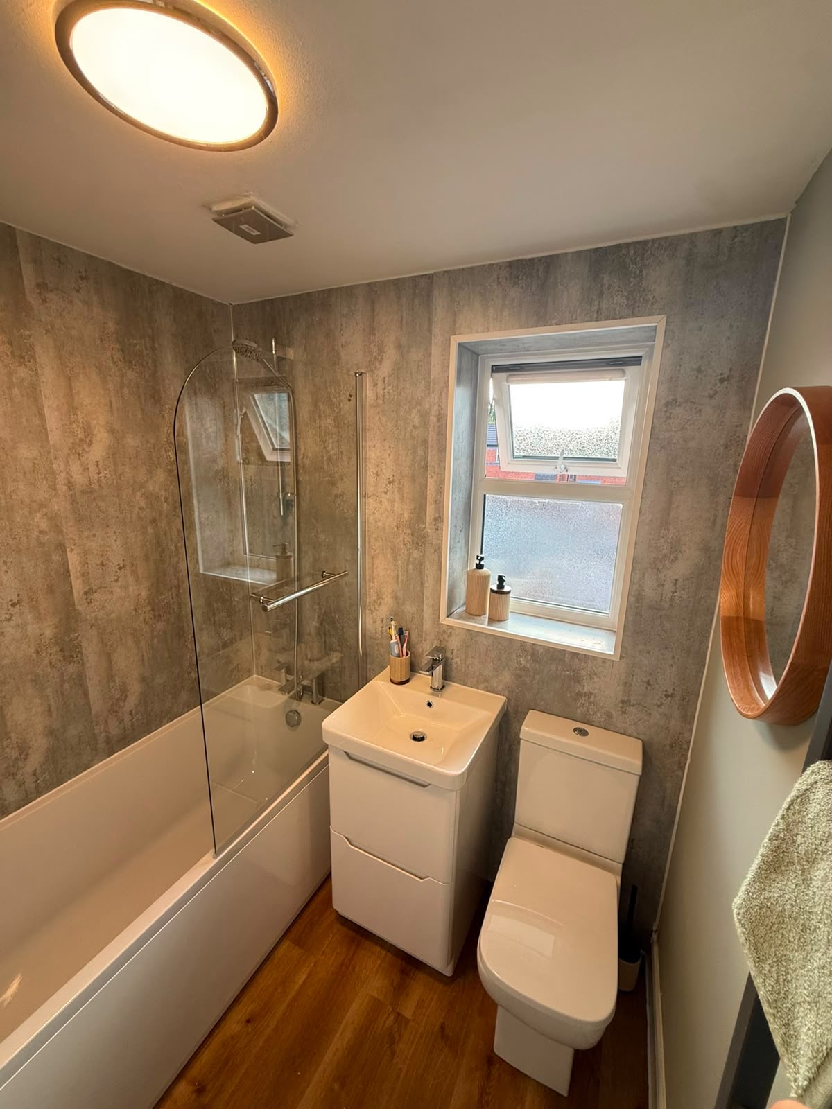 The transformed bathroom: stone-effect panels, new suite, bath with shower screen and wood floor